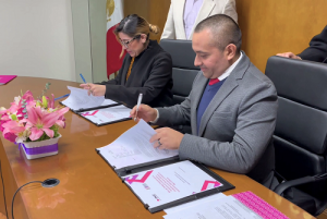 Mujer y hombre sentados detrás de mesa firmando convenio