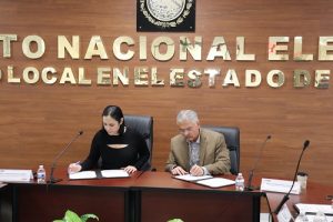 Mujer y hombre sentados detrás de mesa firmando convenio