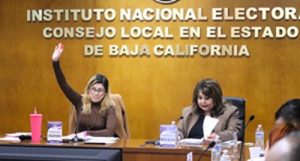 Vocales del INE sentadas durante sesión, una de ellas levantado su mano derecha