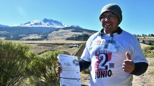 Integrante del INE posando para fotografía, a su espalda paisaje