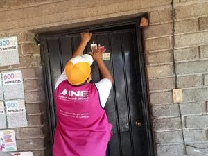 CAE del INE colocando estampa en puerta de domicilio particular