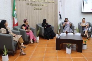 Participantes del foro sentadas en sillones, una de ellas hablando con micrófono