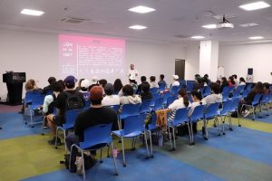 Jóvenes sentados en auditorio durante presentación de integrante del INE