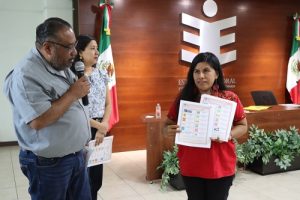 Mujer sosteniendo dos hojas mientras hombre habla a micrófono