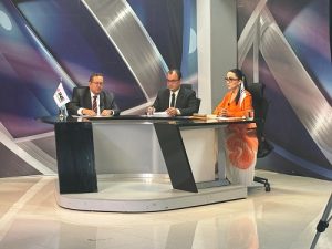 Dos hombres de lentes y con traje sentados junto a mujer de lentes y cabello recogido