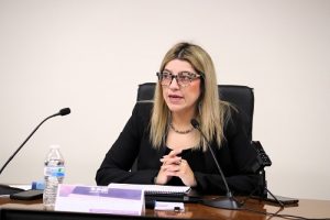 Mujer de lentes sentada hablando a micrófonos
