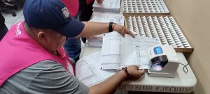 Hombre con gorra y chaleco del INE sosteniendo sobre