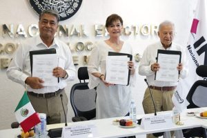 Dos hombres y una mujer, cada uno sosteniendo una copia del convenio firmado