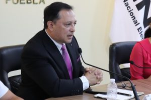 Hombre de traje negro sentado hablando a micrófono