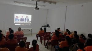 Hombres en prisión preventiva sentados observando una proyección en una pared