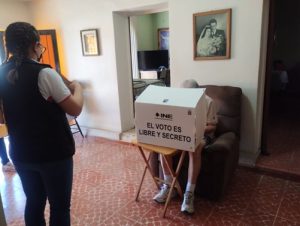 Adulto mayo efectuando su voto desde su casa con asistencia de integrante del INE