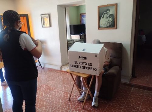 Adulto mayo efectuando su voto desde su casa con asistencia de integrante del INE