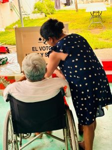 Hombre en silla de ruedas siendo asistido para ejercer su voto