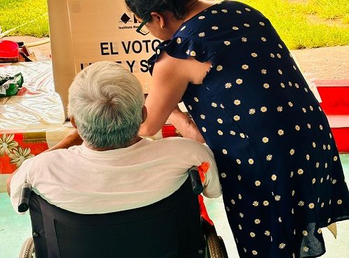 Hombre en silla de ruedas siendo asistido para ejercer su voto