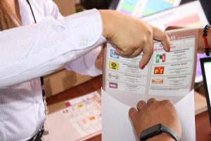 Manos depositando boletas electorales en sobre de color blanco