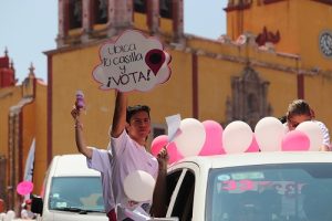Hombre saliendo por ventana de coche con una pancarta en mano