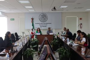 varias personas sentadas alrededor de una mesa rectangular con micrófonos