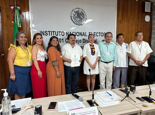 varias personas de pie frente a una mesa con micrófonos