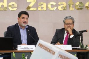 dos hombres sentados frente a una urna de votación