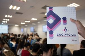 Mano sujetando banner informativo, de fondo sala de juntas difuminada