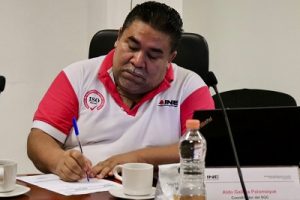 Hombre de bigote cano escribiendo en libreta sobre mesa