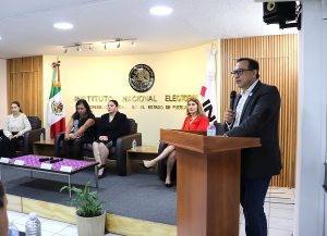 Hombre de lentes hablando en atril, al fondo presidio de presentación