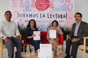 cuatro personas sentadas, dos mujeres sostienen un documento