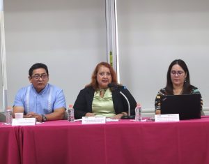 tres personas sentadas frente a una mesa con mantel rosa y un micrófono