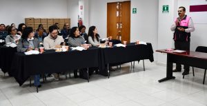 personas sentadas escuchando a un hombre de pie con chaleco rosa