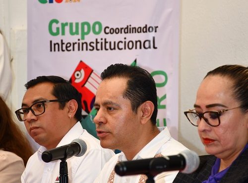 tres personas sentadas frente a dos micrófonos