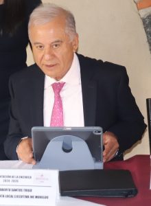 Hombre de pelo cano sentado detrás de mesa con una tablet en sus manos