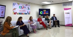 Personas sentadas en un salón con posters de la Consulta Infantil