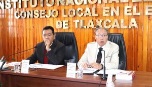 dos hombres sentados atrás de una mesa de madera con micrófono