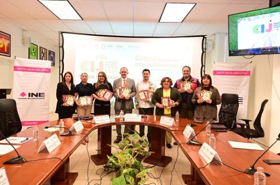 personas de pie frente a una pantalla gigante sosteniendo cuadernillo de colores