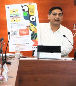 Hombre de camisa blanca sentado, sosteniendo cártel de la Consulta Infantil y Juvenil 2024