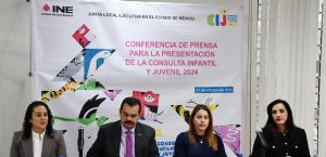 Autoridades del INE sentadas detrás de mesa, a su espalda cártel de la Consulta Infantil y Juvenil 2024