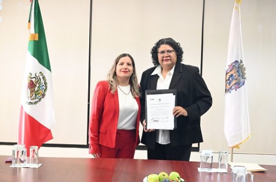 Mujer de saco rojo y mujer de lentes sosteniendo reconocimiento