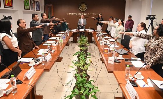 Integrantes del INE de pie durante sesión, algunos de ellos extendiendo su brazo derecho