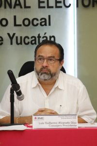 Hombre de barba canosa y lentes, sentado detrás de mesa