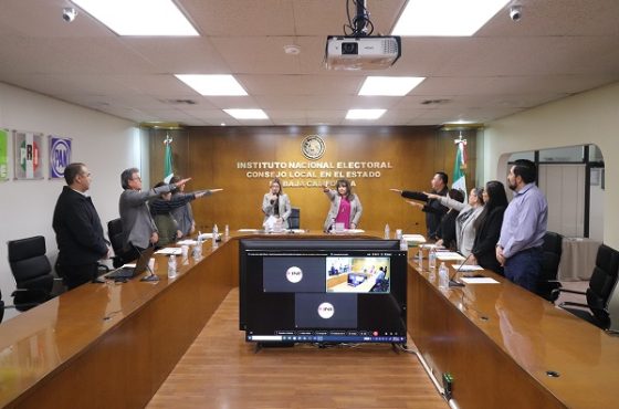 Integrantes del INE de pie estirando su brazo derecho