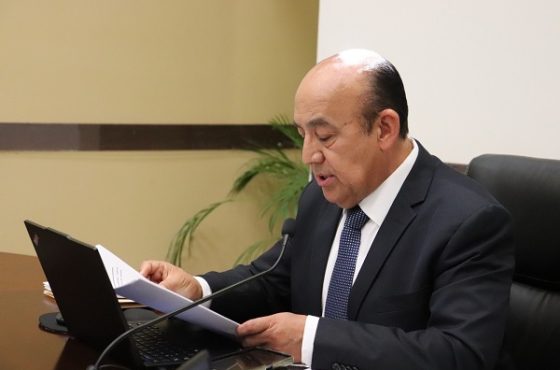 Hombre semi calvo sentado detrás de escritorio hablando a micrófono