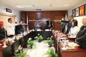 Integrantes del INE de pie estirando su brazo derecho