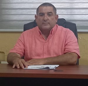 Hombre viendo de frente a la cámara, sentado con las manos en la mesa