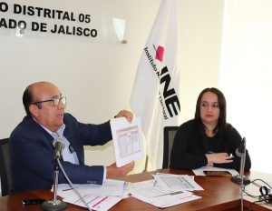 Dos personas sentadas, uno de ellos hombre muestra un documento