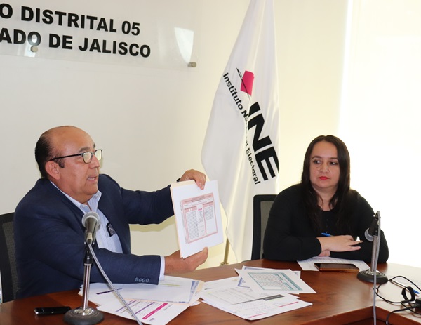 Dos personas sentadas, uno de ellos hombre muestra un documento