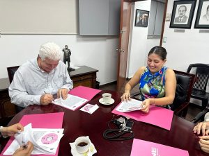 Dos personas sentadas en una mesa firmando el convenio