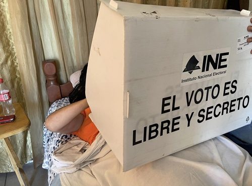 Persona en cama realizando su voto en mampara del INE
