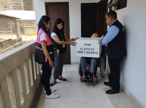 Tres personas del INE platicando con una persona en silla de ruedas