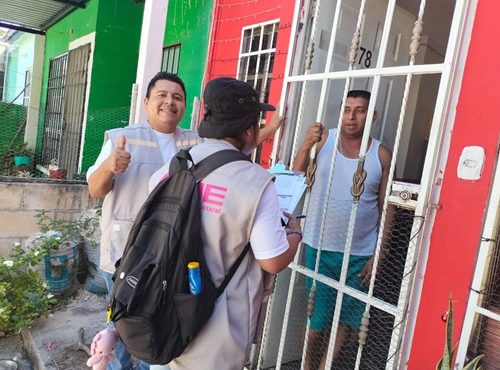 dos trabajadores del INE platicando con una persona en su domicilio