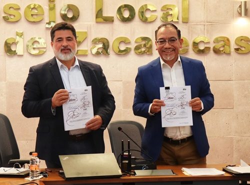 Dos hombres de pie sosteniendo un documento, mirando al frente